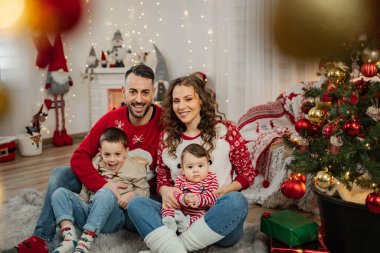 Neşeli aile, süslü bir Noel ağacının yanında yerde otururken gülümsüyor.