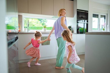 Bir anne, parlak bir mutfakta çocuklarıyla dans eder..