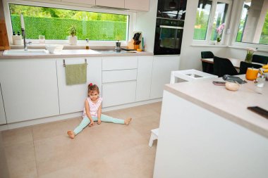Çocuk neşeli bir şekilde güneşli bir mutfakta yerde oturuyor..