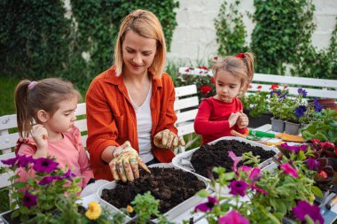 Dışarıda neşeli anlar paylaşan üç kişi çiçek diker..