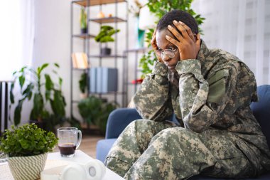 Depresyondaki Afro-Amerikan askeri travma sonrası stres bozukluğundan muzdarip. Evdeki koltukta oturuyor.