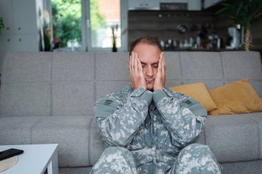 Depresyondaki asker evinde oturmuş elleriyle yüzünü kapatıyor. Travma sonrası stres bozukluğu yaşıyor.