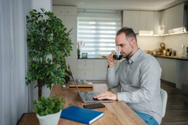Adam işine odaklanıyor, kahve içiyor ve uzaktan çalışıyor.