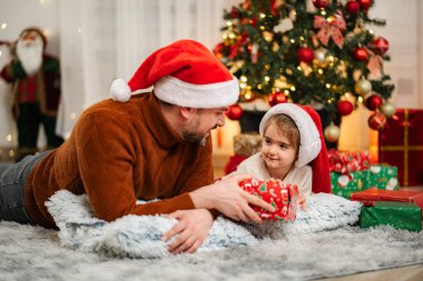 Baba ve küçük kızı Noel kutlaması sırasında halının üzerinde yatıp birbirlerine hediye veriyorlar.