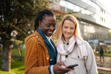 İki gülümseyen kadın meslektaşım, içeriğe bakarak akıllı telefon ekranını paylaşıyor.