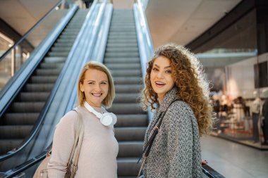 İki yetişkin kadın arkadaş modern bir alışveriş merkezinde vakit geçiriyorlar.