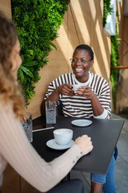 Kadın arkadaşlar gülümsüyor ve konuşuyorlar, kahve masasında kahve içiyorlar.