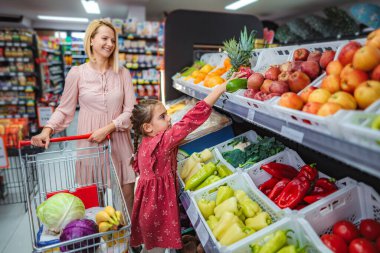 Anne ve kız süpermarket koridorunda taze meyve ve sebze seçiyorlar.