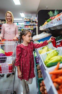 Markette annesiyle kırmızı biber toplayan bir kız.