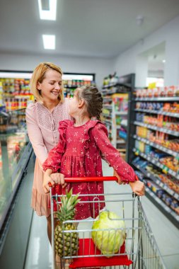 Anne ve kızı bir alışveriş arabasını iterken gülümsüyor.