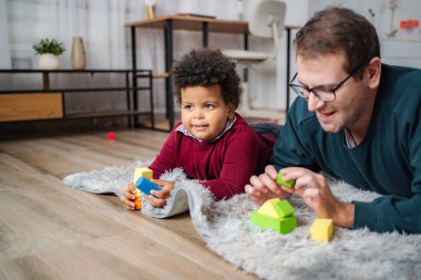 Baba ve çocuk evdeki halıda oyuncaklarla kaynaşıyor.