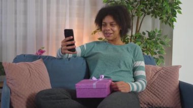 Doğum günü hediyesi kutusunu tutan ve telefonunda video konferansı yapan mutlu bir kadın.