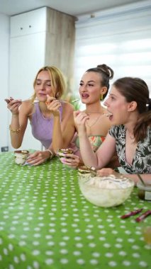 Üç genç kadın mutfak masasında fıstıklı krema tatlısı yiyorlar.