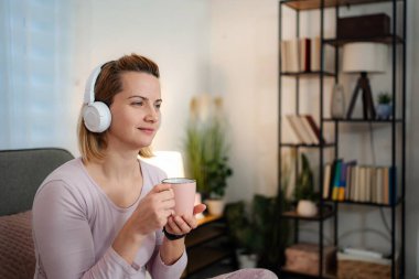 Genç bir kadın, kulaklıklar ve kupayla sessiz vakit geçiriyor.
