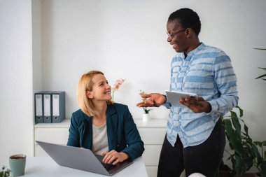 İki iş kadını bilgisayar ve dijital tablet kullanarak çalışmayı tartışıyor, gülümsüyor
