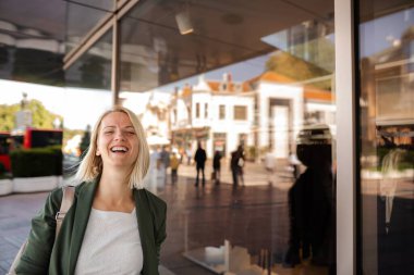 Şehirde gülen bir kadın, cam duvarda görünen insanların ve binaların yansımaları.
