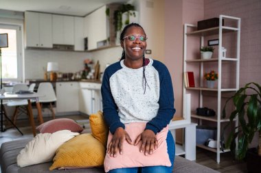 Genç bir kadın kanepede dinleniyor, evde gülümsüyor.