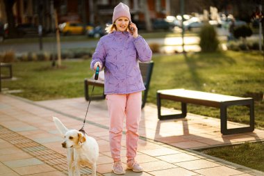 Kadın ve köpek cep telefonuyla konuşurken sonbahar yürüyüşünün tadını çıkarıyorlar.