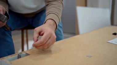 Marangoz mobilya montajı yapıyor, çekiçle tahta çivi çakıyor.