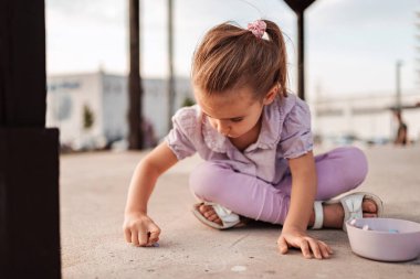 Anaokulu kızı kaldırıma tebeşirle resim çiziyor.