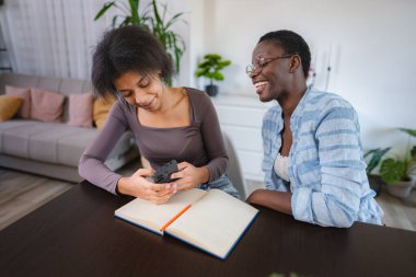 İki neşeli genç kadın bir masada oturmuş, akıllı telefondan bir şeye bakarken bir anlık kahkaha atıyorlar.