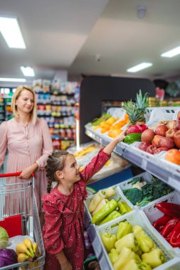 Anne ve kız süpermarketten taze meyve ve sebze seçiyorlar.