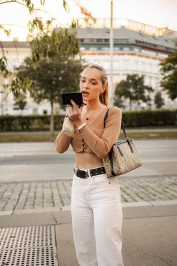 Genç bir kadın dışarıda aynaya bakarken ruj sürüyor.