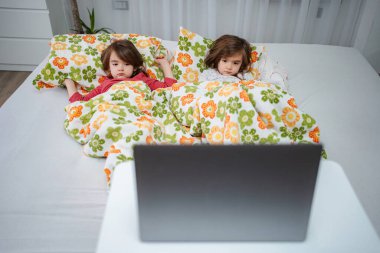 Evde yatıp dizüstü bilgisayara bakan tek yumurta ikizi kızlar.