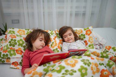 Genç kızlar, erken okuma yazma ve çocukluk bağlarını benimseyerek yatakta masal zamanı geçiriyorlar.