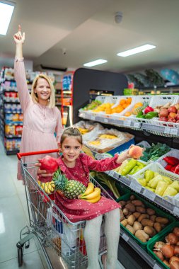 Anne ve kızı markette sağlıklı meyve seçiminin tadını çıkarıyorlar.