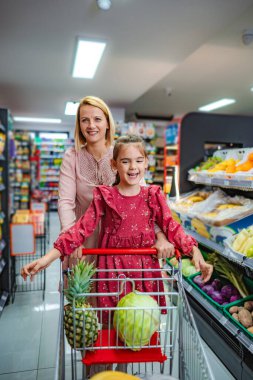 Mutlu anne ve kız marketten taze meyve ve sebze alıyor.