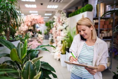 Çiçekçi, çiçek ve çiçeklerle çevrili bir çiçekçiden sipariş alırken notlar alıyor.