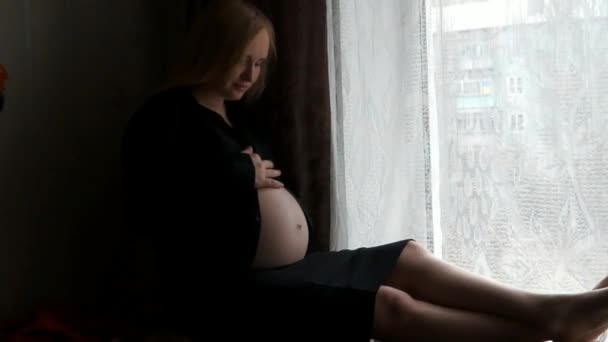 Een zwangere vrouw zitten in de buurt van het venster. — Stockvideo