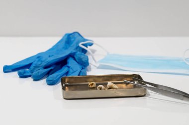 Cımbız, tıbbi maske ve eldivenlerin yanında metal bir tepside yatan hastalıklı dişler. Diş hekimliği. Ameliyat..