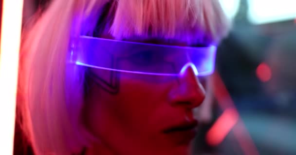 The blonde in neon glasses sits in a futuristic room and looks out the window. — Stock Video