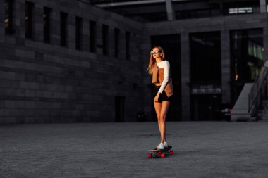 Genç bir kadın şehirde uzun bir sörf tahtasına biniyor..