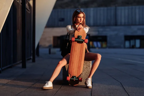 Mujer joven monta un longboard alrededor de la ciudad. — Foto de Stock