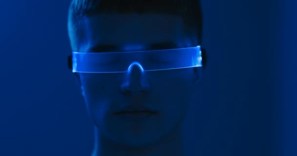 Neon gözlüklü, gözleri kapalı genç bir adamın portresi. Mavi neon oda. — Stok video