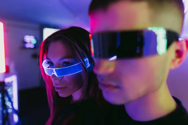 Ett par personer som står under neonljus. Futuristiska glasögon. — Stockfoto