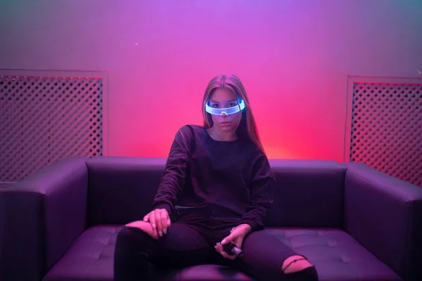 Neonnoir. Egy neon szobában ülő nő neon szemüvegben.. — Stock Fotó