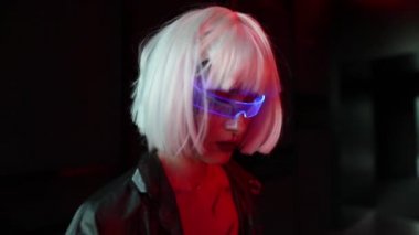 Siber gözlüklü bir kadın karanlıkta neon ışıklarıyla dikiliyor..