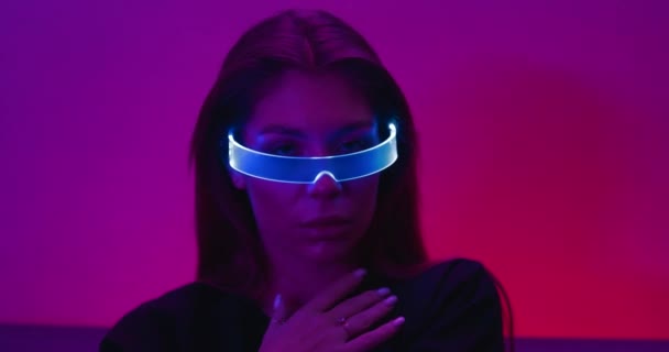 Weibliches Cyberpunk-Videoporträt. Frau in einem Neon-Raum mit glühender Brille. Es gibt eine Wirkung von Lärm, Getreide. — Stockvideo