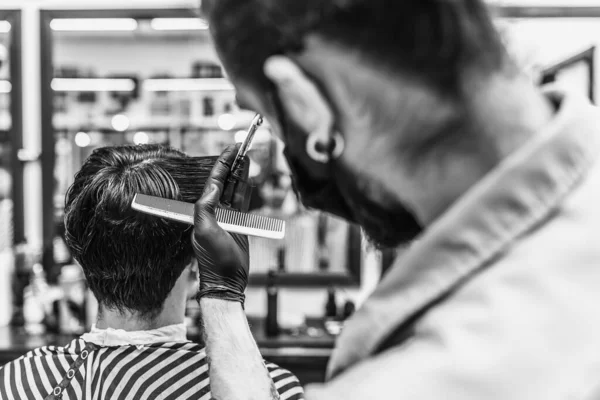 Barbeiro faz um corte de cabelo e estilo de cabelo em uma barbearia, salão de beleza. — Fotografia de Stock