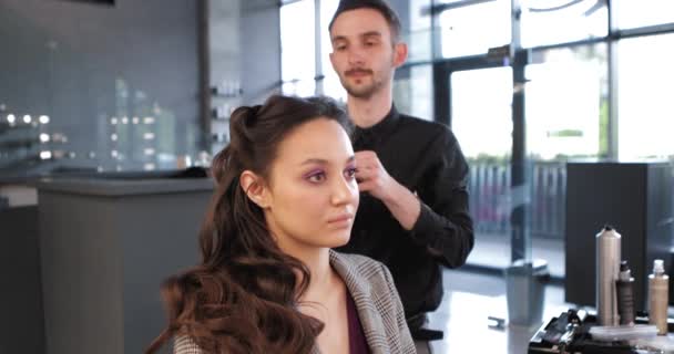 Cabeleireiro faz um penteado retro elegante para uma jovem mulher com cabelo escuro. — Vídeo de Stock