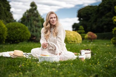 Bir kadın yemyeşil bir bahçede battaniyenin üzerinde dinleniyor..