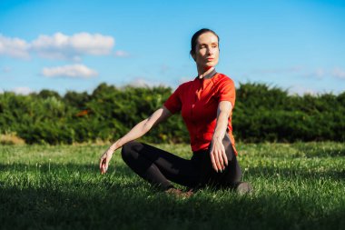 Güneşli bir günde, yoga pozunda çimlerin üzerinde oturan bir kadın. Doğayı seviyor ve esnetiyor..