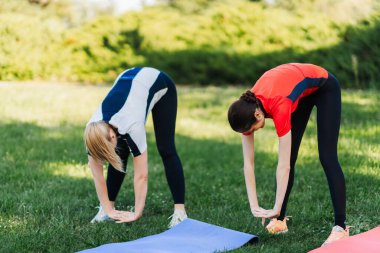 Sabahları çimenli bir park alanında iki kadın esneme egzersizleri yapıyor..