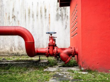 Parlak kırmızı endüstriyel su borusu. Geniş manuel vanası var. Sıkıntılı beyaz bir duvara karşı ve hararetli kırmızı bina dışı. Güvenlik, tesisat, yangın söndürme.
