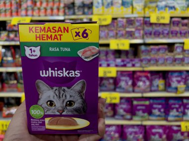 Perak, Malezya - 16 Aralık 2025: Bir marketin evcil hayvan reyonunda mor bir Whiskas tuna balığı çeşnili kedi maması taşıyan bir kişi.