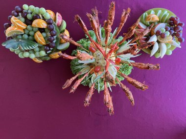 İki sanatsal meyve tabağıyla çevrili oyulmuş sebze tabağının etrafına yerleştirilmiş kızarmış karideslerin yer aldığı ayrıntılı bir açık büfe ya da düğün yemeği sergisi..